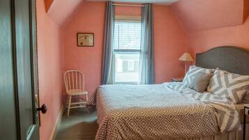 Een slaapkamer met een bed, een stoel, een raam met gordijnen en een plafondventilator.