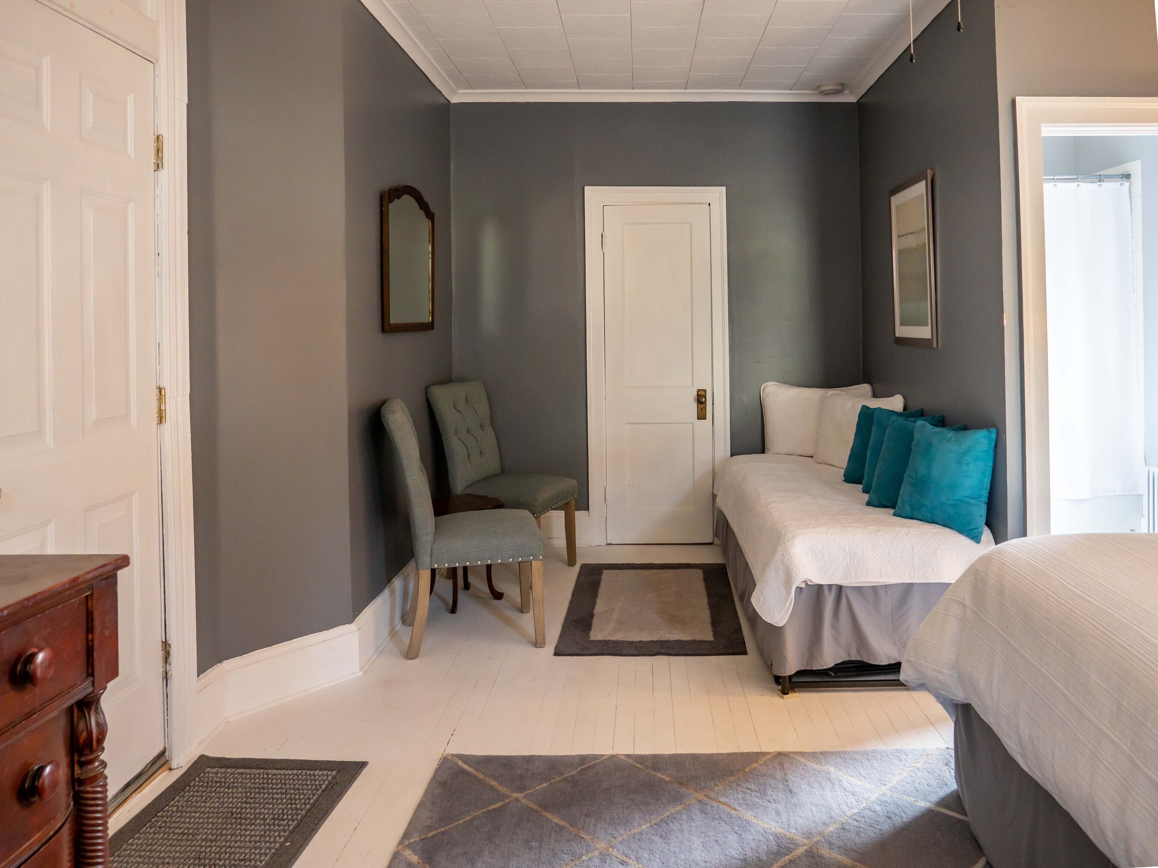 A bedroom with a bed, a chair, a door, and a dresser.