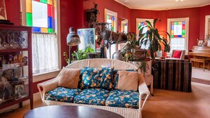 A cozy living room with a wicker sofa, a round coffee table, and a piano in the background. - River Run Bed and Breakfast (Fleischmanns)