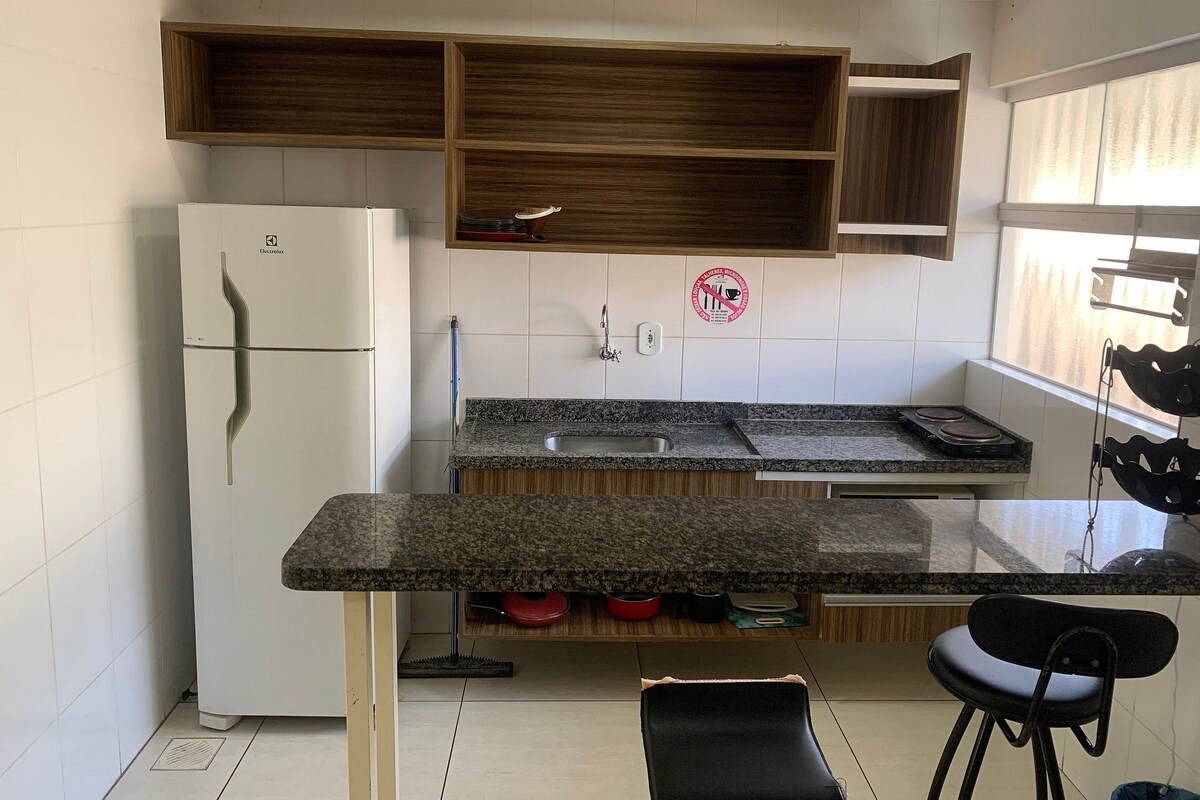 Una cocina con refrigerador blanco, encimeras de granito, armarios de madera, un lavamanos y una ventana con persianas.