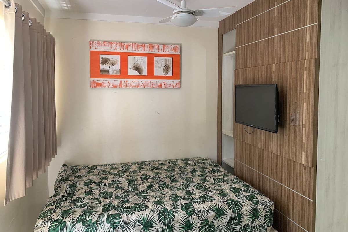 A bedroom with a bed, a ceiling fan, a TV, and a wall with a wooden panel design.