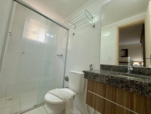 Un baño moderno con cabina de ducha de vidrio, inodoro blanco y encimera de granito con mueble de madera.