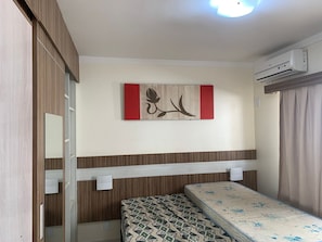 Une chambre à coucher comprenant un lit, un climatiseur fixé au mur, une armoire en bois, un miroir et un objet décoratif.