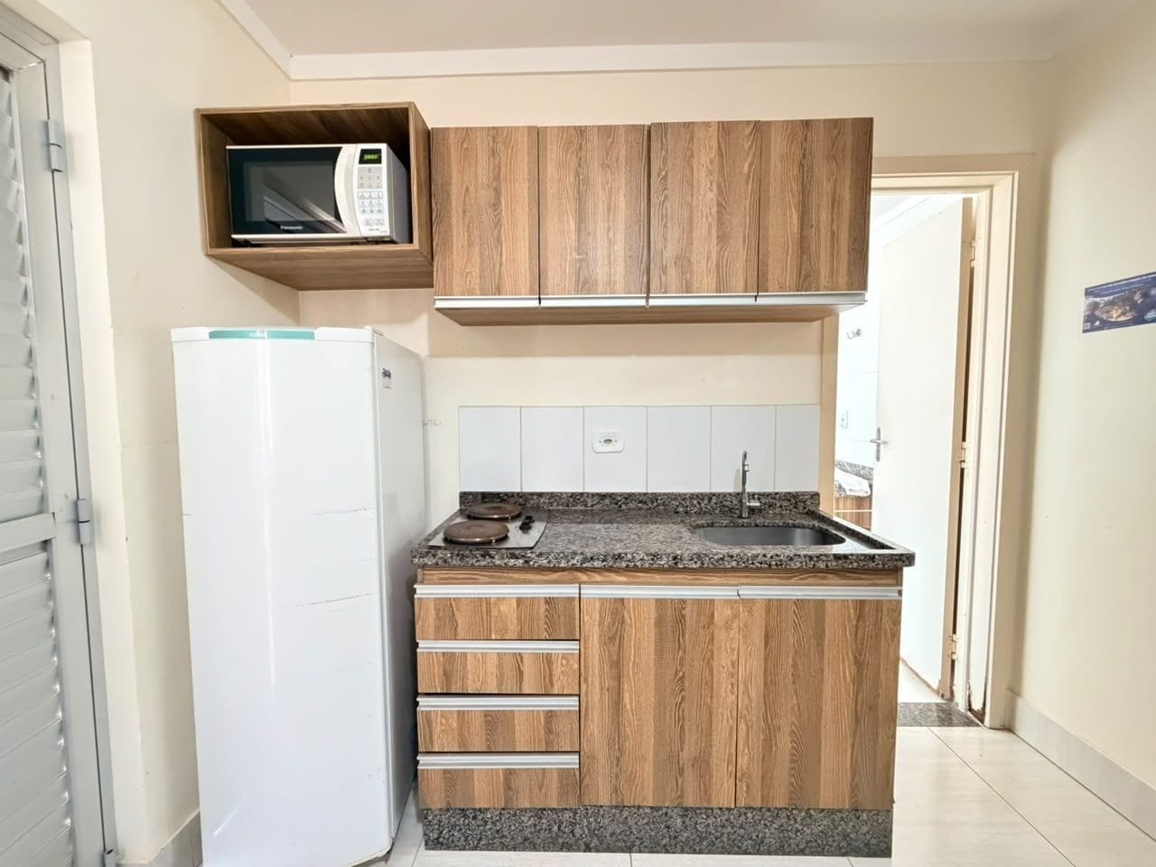 A compact kitchen with wooden cabinets, a built-in microwave, a refrigerator, and a granite countertop.