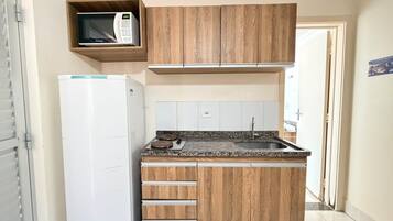 A compact kitchen with wooden cabinets, a built-in microwave, a refrigerator, and a granite countertop.