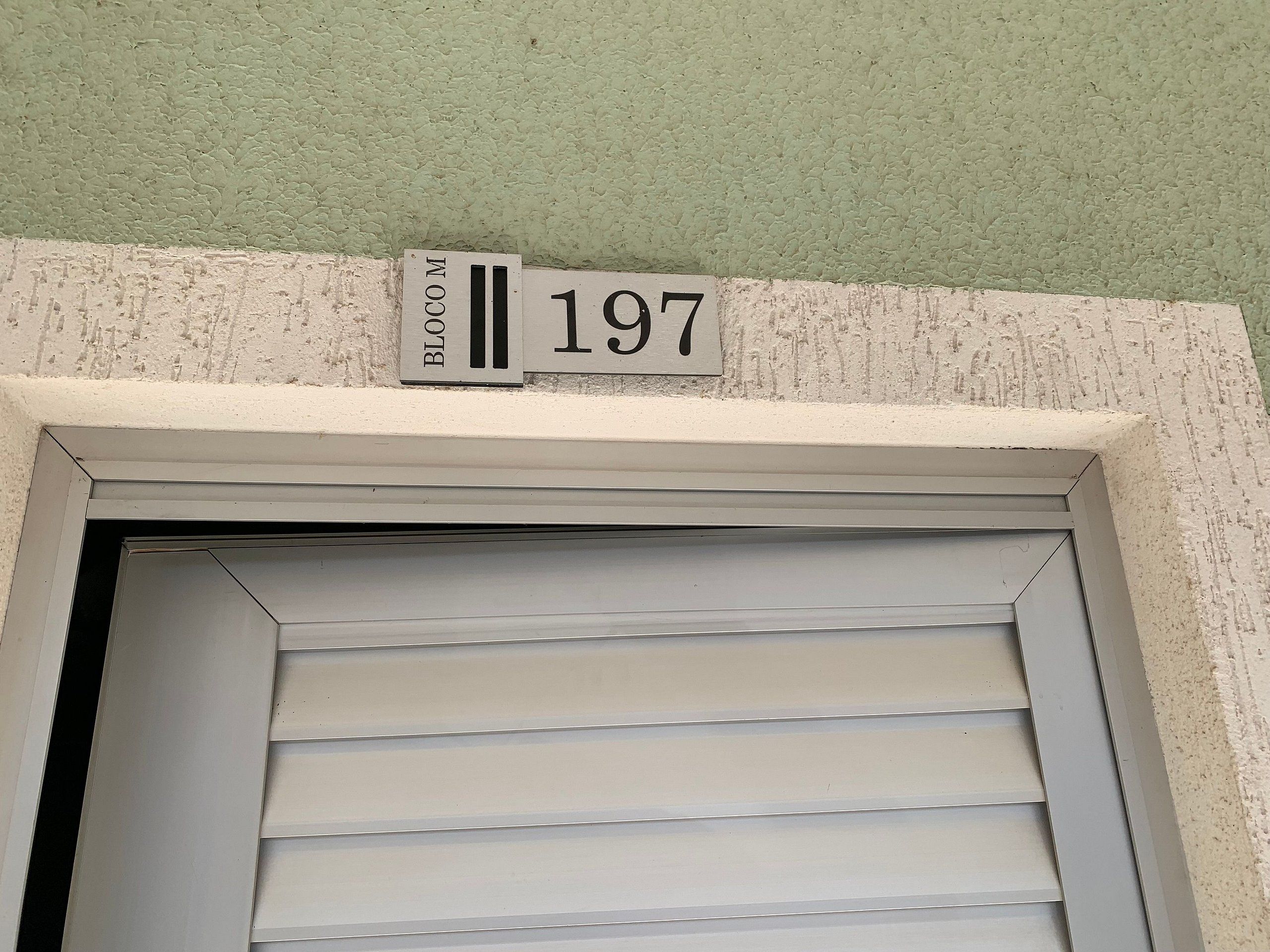 Une entrée d’immeuble avec une porte blanche, un mur vert à texture et une enseigne indiquant l’adresse « 197 BLOOM CO MI ».