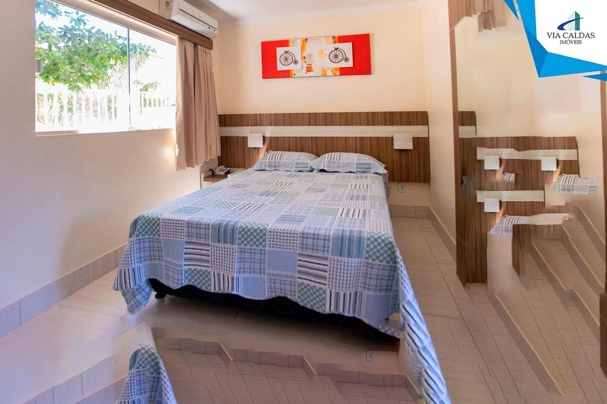 A bedroom with a bed, a window with curtains, a wall-mounted artwork, and a staircase.