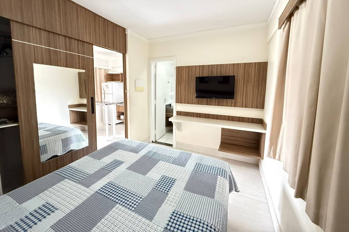 A hotel room with a bed, a TV mounted on the wall, and a wardrobe.
