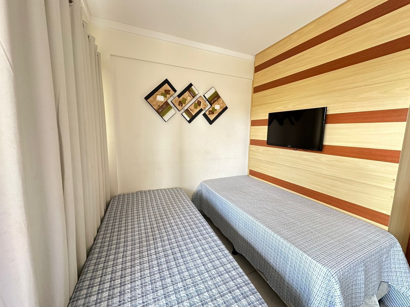 A small room with two single beds, a TV mounted on a wooden wall, and three framed pictures.