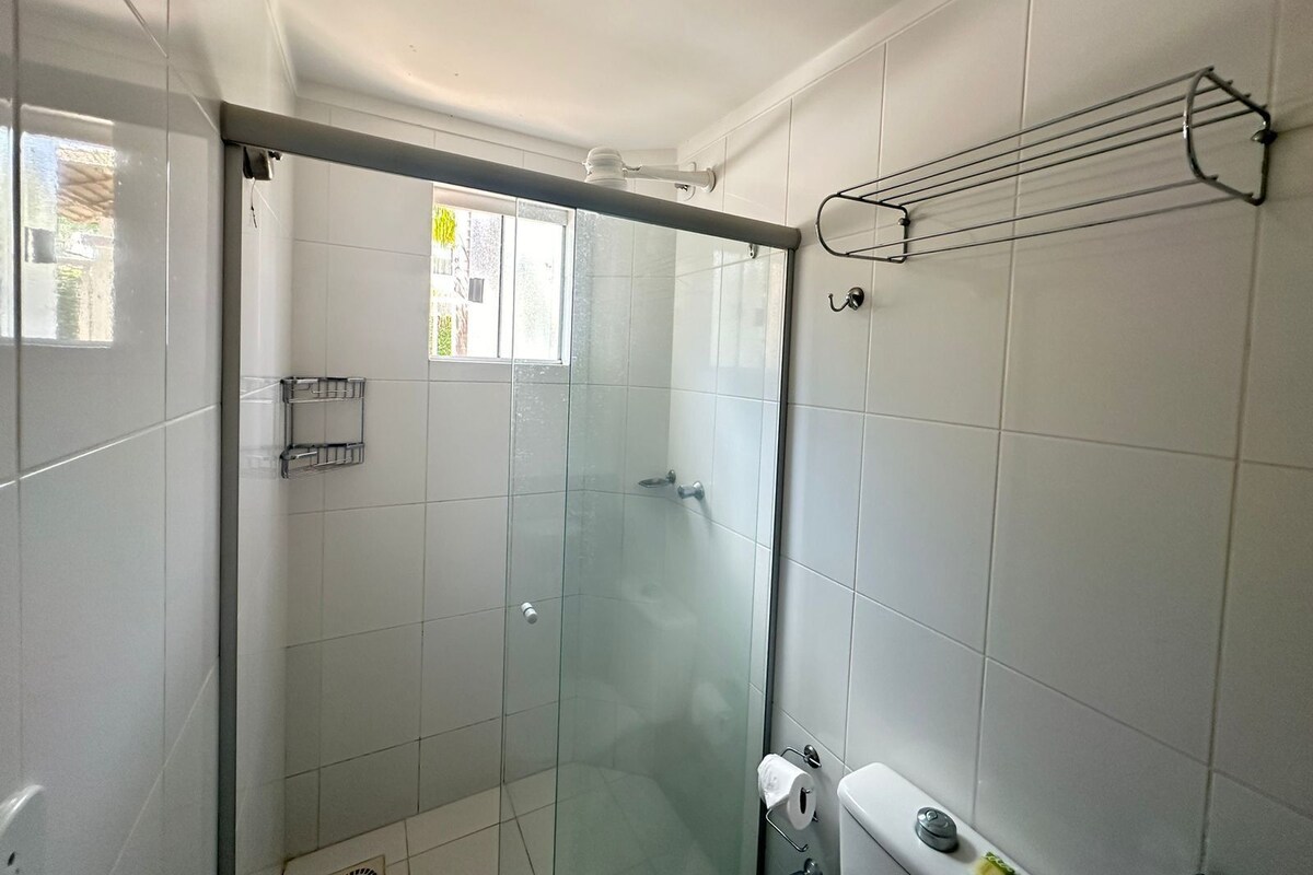 Un baño moderno con azulejos blancos, ducha con cerramiento de vidrio, dispensador de papel higiénico y perchero para toallas.