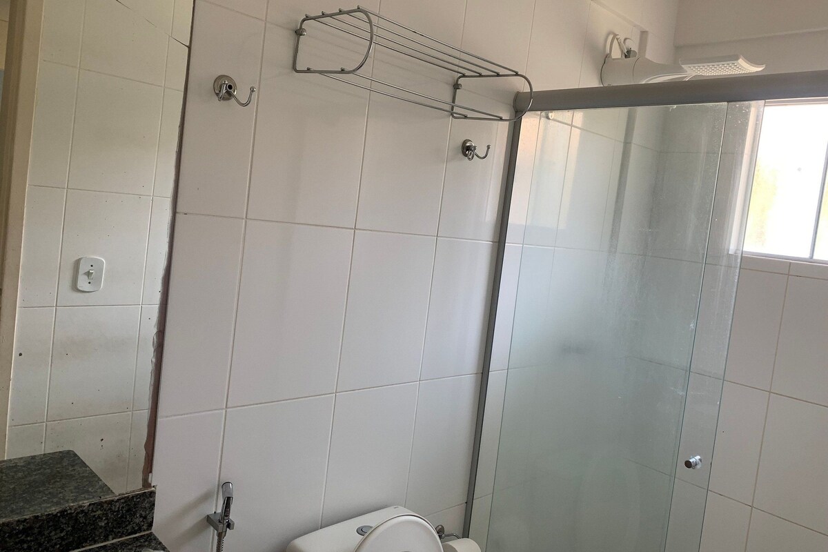 Un baño con paredes de azulejos blancos, cabina de ducha, inodoro y lavabo con encimera de granito.