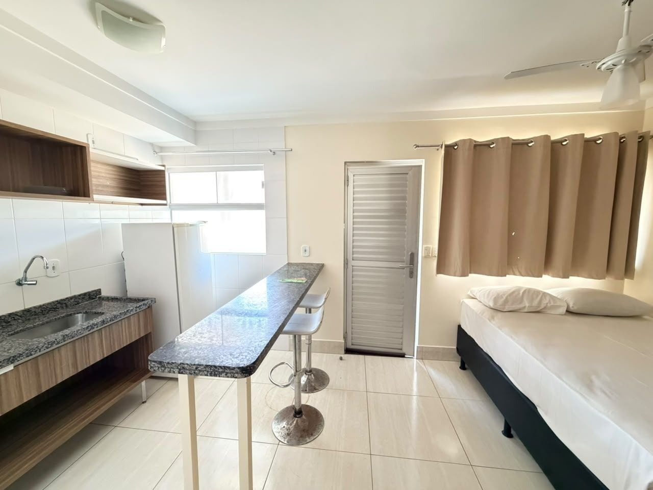A compact room with a kitchenette, a bed, and a bathroom.