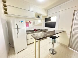 Cozinha compacta com geladeira embutida, fogão a gás e bancada pequena.