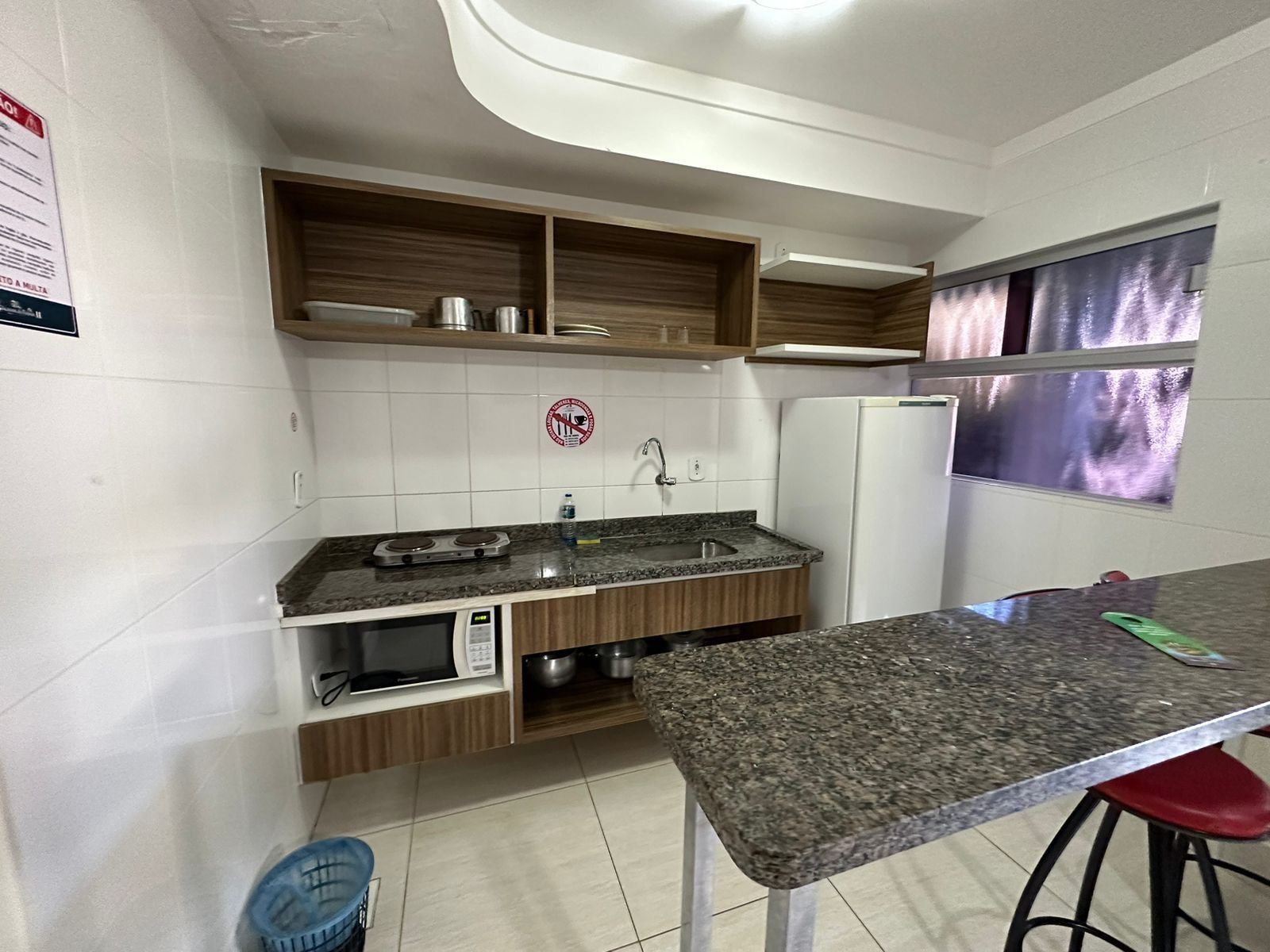 Uma cozinha compacta com micro-ondas embutido, pia e prateleiras de madeira acima.