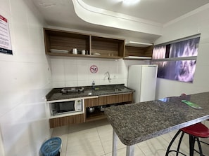 Uma cozinha compacta com micro-ondas embutido, pia e prateleiras de madeira acima.