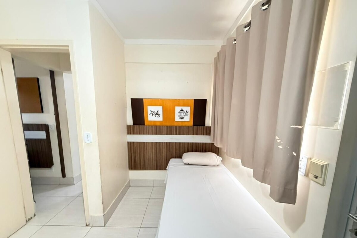 Habitación de hotel con una cama individual, un pequeño rincón de descanso con una mesa y un estante en la pared con dos cuadros.