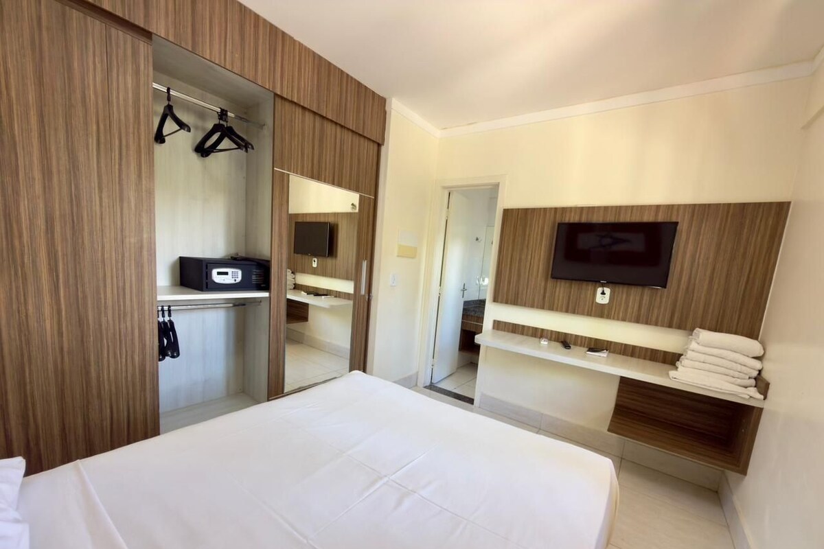 Una habitación de hotel con cama, armario, espejo, televisión y estante con toallas.