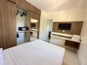 Una habitación de hotel con cama, armario, espejo, televisión y estante con toallas.