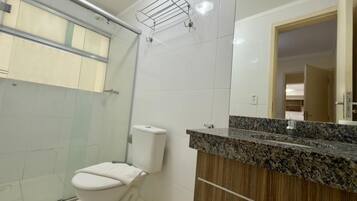 A bathroom with a toilet, a shower, a sink with a granite countertop, and a mirror.