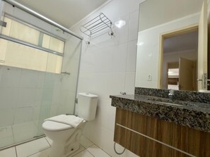 Un baño con inodoro, ducha, lavamanos con encimera de granito y espejo.