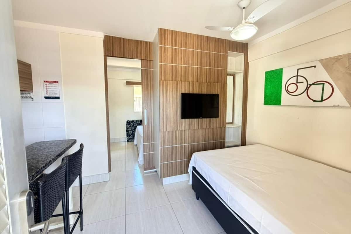 A hotel room with a bed, a TV, a desk with a chair, and a wall-mounted artwork.
