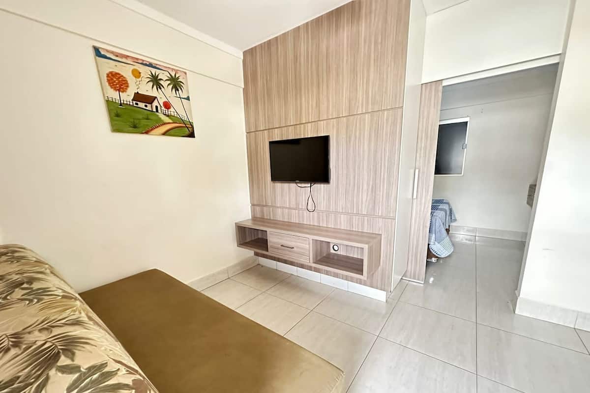 A bedroom with a bed, a TV mounted on a wooden wall, a painting, and a wardrobe.