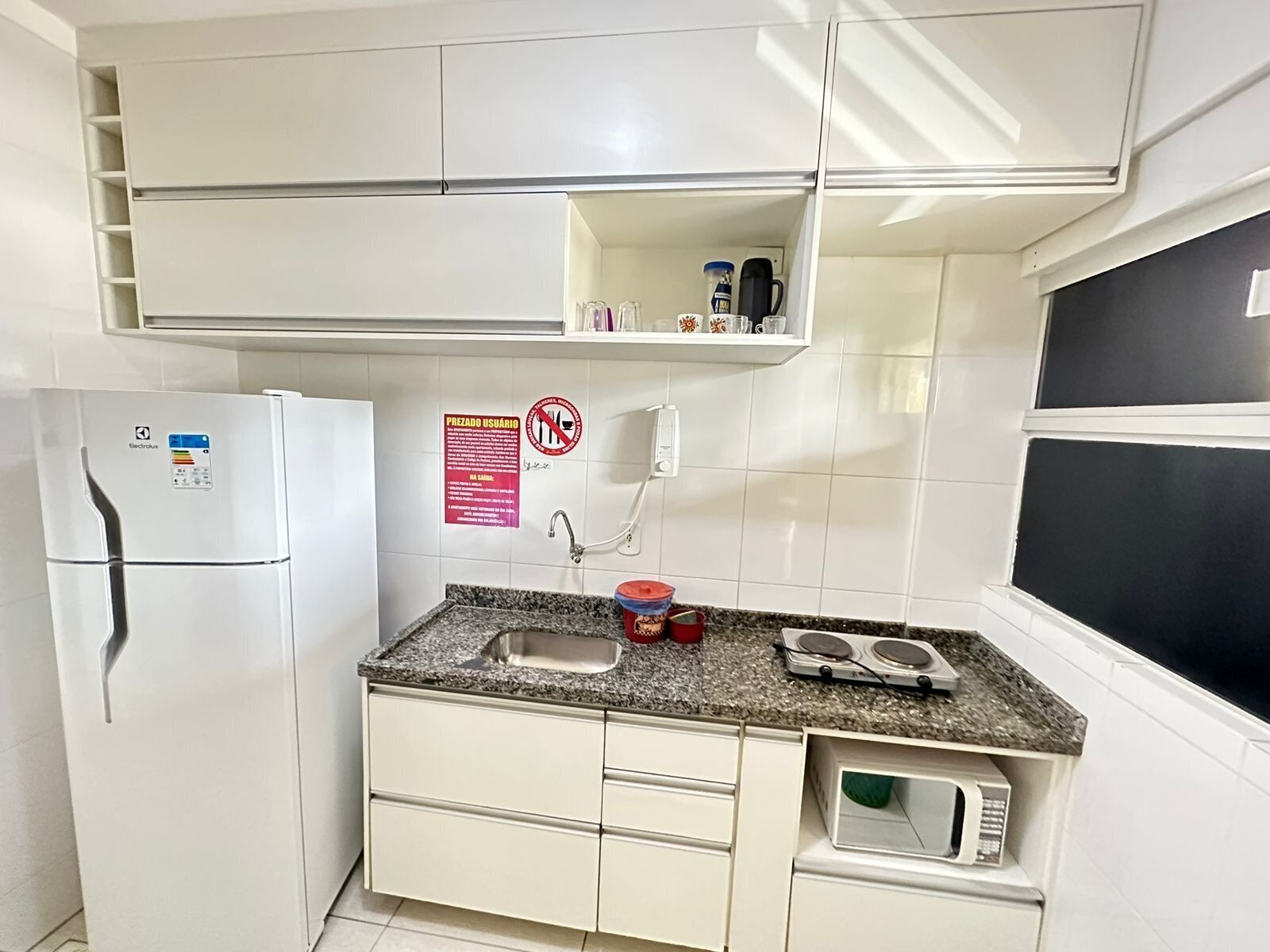 A compact kitchen with a refrigerator, microwave, sink, and a small countertop with a kettle and a coffee maker.
