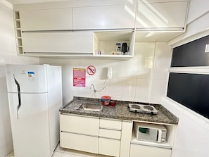 Cocina compacta con refrigerador, microondas, fregadero y una pequeña encimera con hervidor y cafetera.
