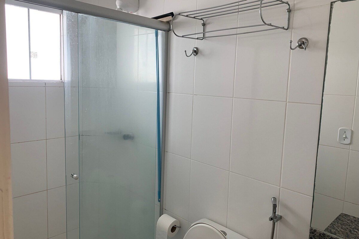 Un baño con puerta de vidrio, zona de ducha, inodoro y un perchero para toallas.