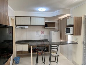 A compact kitchen with a built-in microwave, a refrigerator, and a sink. There are two bar stools and a small trash bin. - Lacqua DiRoma II Via Caldas (Caldas Novas)