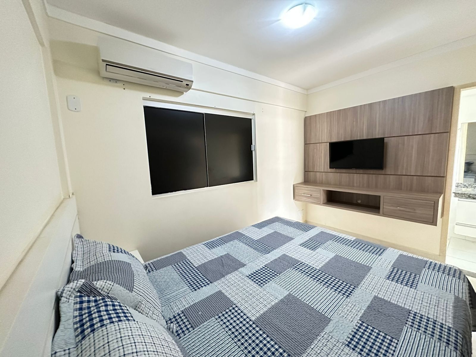 Um quarto com uma cama, uma TV fixada na parede e um armário embutido de madeira.