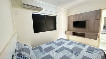 Um quarto com uma cama, uma TV fixada na parede e um armário embutido de madeira.