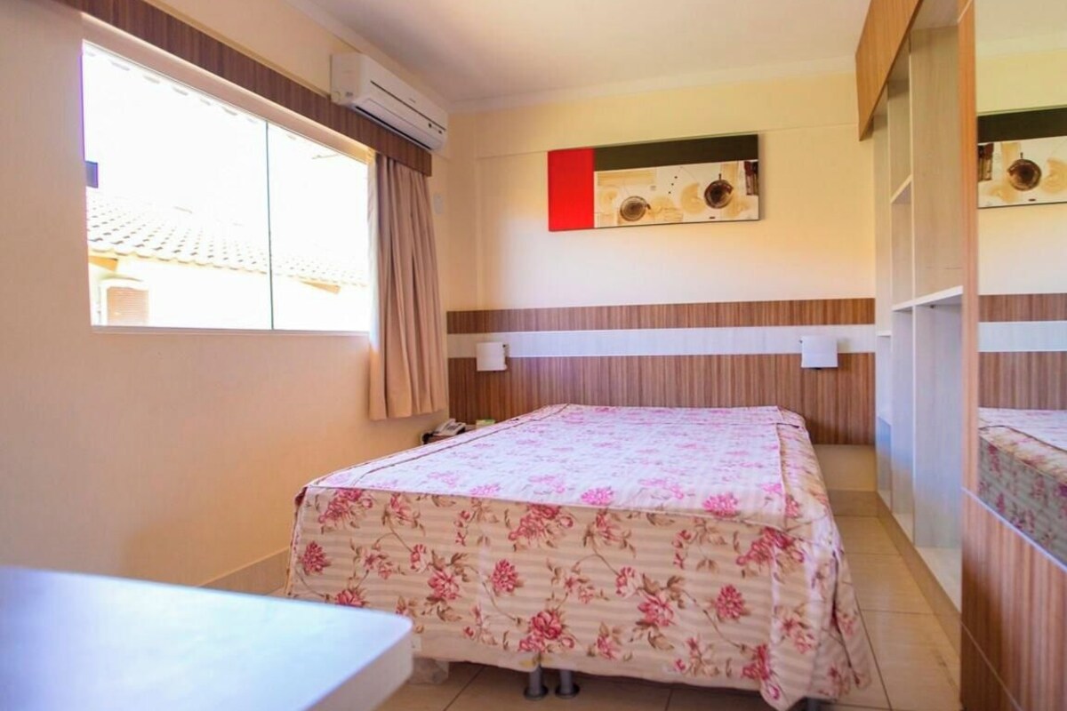 Habitación de hotel con cama, escritorio, ventana y aire acondicionado de pared.