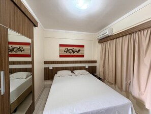 Habitación de hotel con cama, armario, espejo, aire acondicionado montado en la pared y ventana con cortinas.