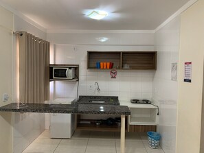 Cocina compacta con microondas integrado, lavamanos y un refrigerador pequeño.