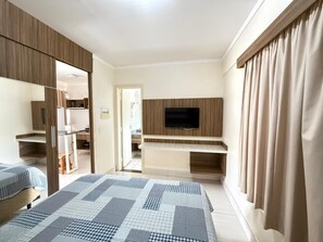 Habitación de hotel con dos camas, un televisor montado en un panel de madera, un escritorio y un armario.