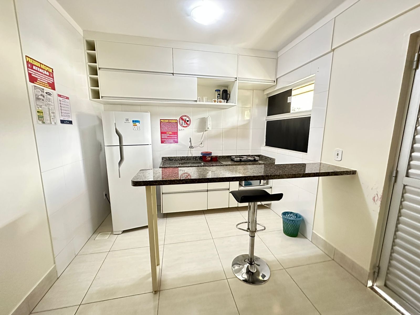 A small kitchen with white cabinets, a refrigerator, a sink, and a bar stool.