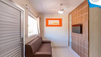 A room with a sliding door, a brown sofa, a ceiling fan, a framed picture on the wall, and a TV mounted on a wooden panel wall.
