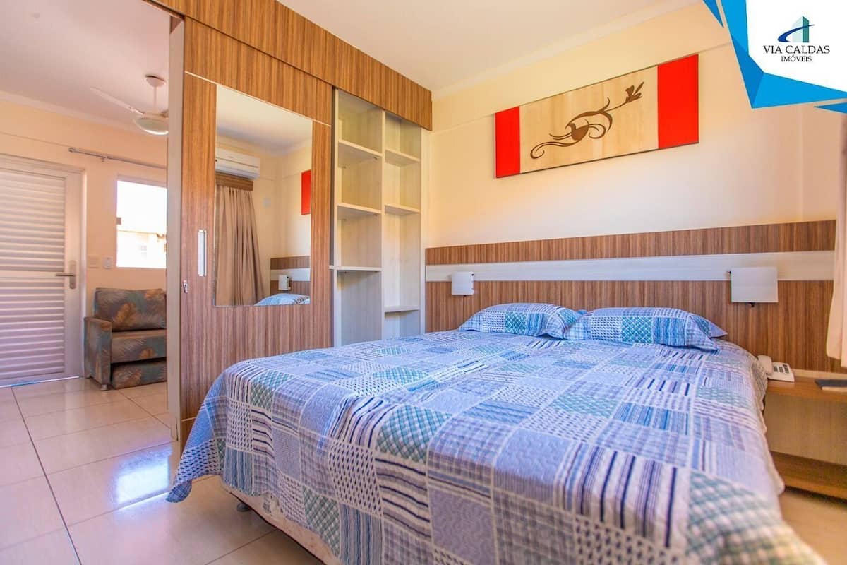 A bedroom with a bed, a wardrobe, a mirror, a nightstand, and a wall-mounted artwork.