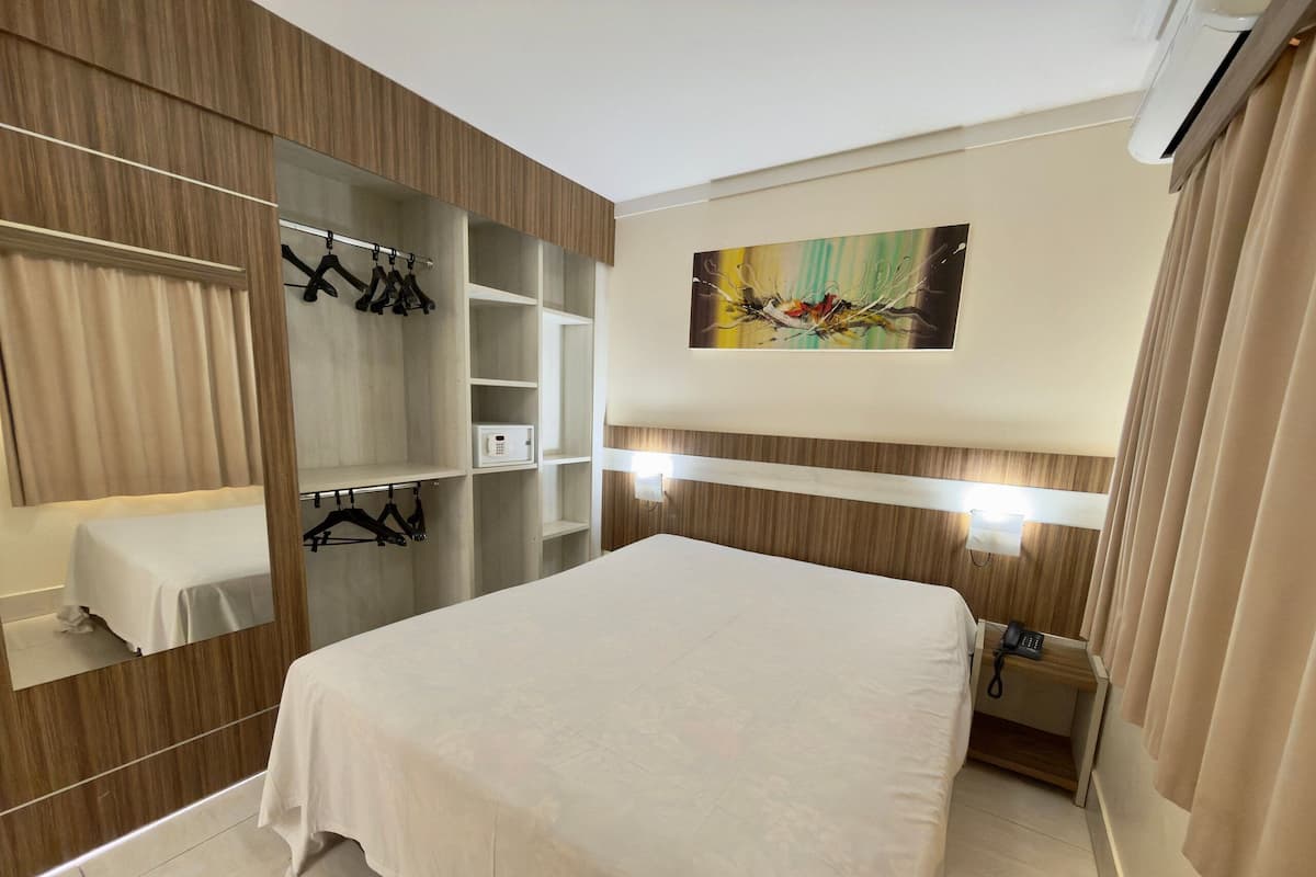 A hotel room with a bed, a wardrobe, a bedside table, a mirror, and a painting on the wall.