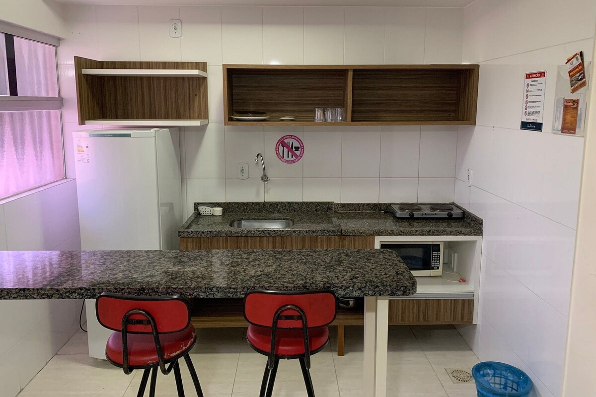 Una cocina compacta con encimera de granito, dos sillas rojas, un microondas y un refrigerador.