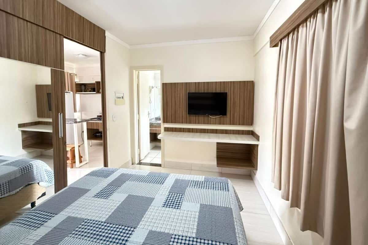 A hotel room with two beds, a TV mounted on a wooden panel, a desk, and a wardrobe.