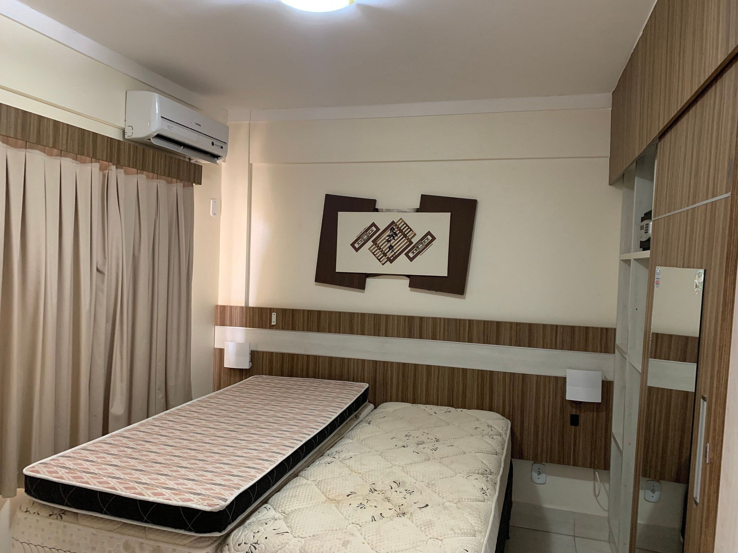 A room with a bed, an air conditioning unit, a wall-mounted light, and a decorative piece.