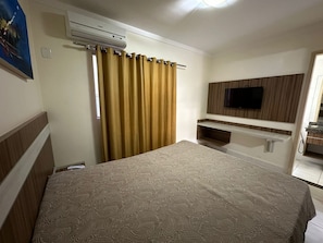 Ein Hotelzimmer mit Bett, Klimaanlage, an der Wand montiertem Fernseher und einem durchgegangene Tür sichtbaren Badezimmer.