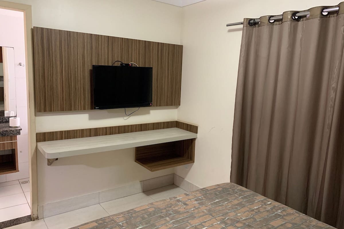 A room with a TV mounted on a wooden panel wall, a white shelf below, and a bed with a brick-patterned headboard.