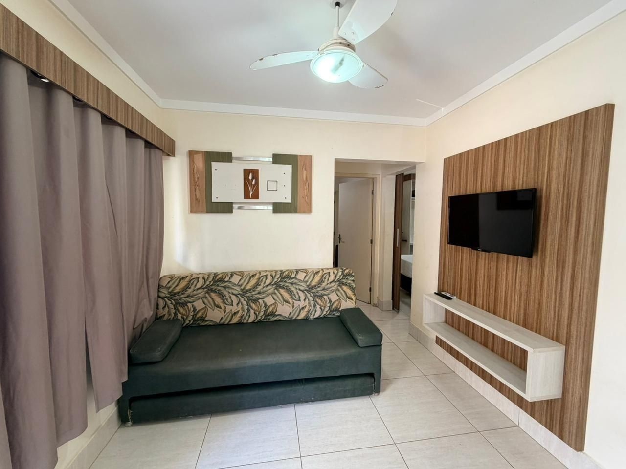 Sala de estar com sofá, televisão, ventilador de teto e prateleira para TV na parede.