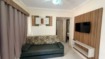 Sala de estar com sofá, televisão, ventilador de teto e prateleira para TV na parede.