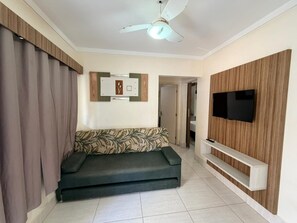 Una sala de estar con sofá, televisor, ventilador de techo y estante para la televisión en la pared.