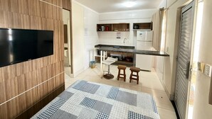 A compact kitchen with a flat-screen TV, wooden cabinets, a marble countertop, and a patterned rug. - Lacqua DiRoma II Via Caldas (Caldas Novas)