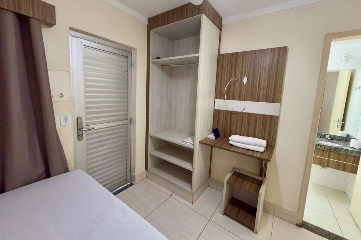 Habitación de hotel con cama, armario, mesita con toalla y espejo.